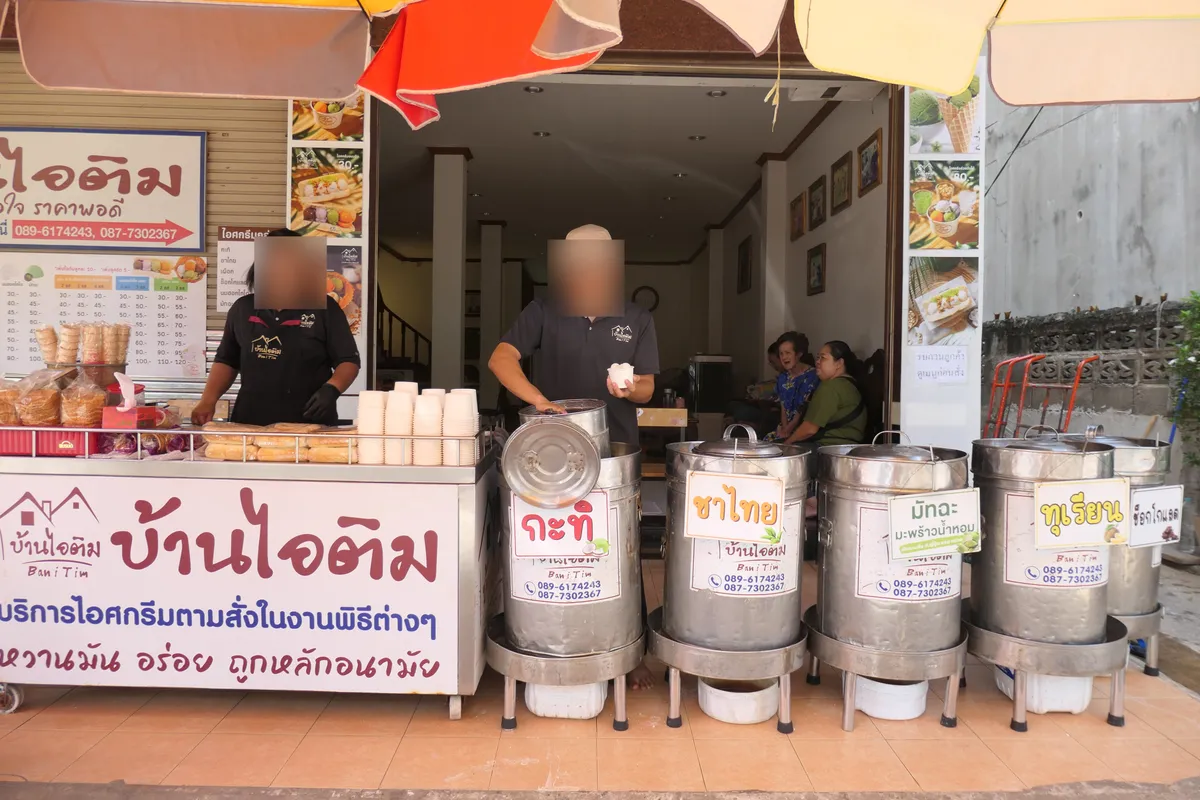 The front of Ban i Tim with flavour signs for coconut, Thai tea, matcha, durian and chocolate, and staff behind the counter
