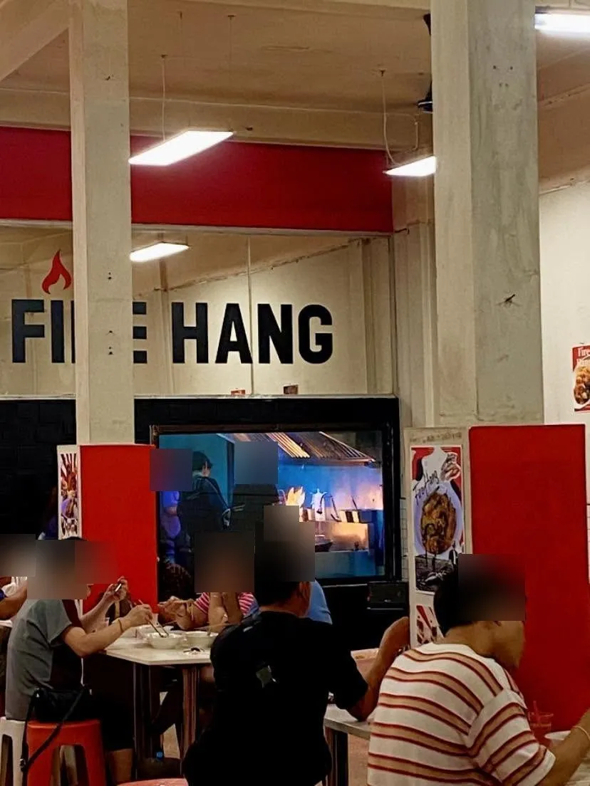 มุมทานอาหารภายในร้าน มีป้าย FIRE HANG และครัวเปิดหลังกระจก ลูกค้ากำลังนั่งทานอาหาร